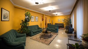 Um hall de hotel com sofás verdes, uma mesa de centro e uma grande planta em vaso.