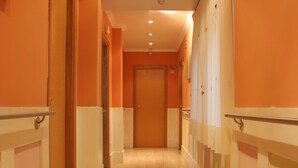 Corredor com piso de madeira e paredes laranja, levando a uma porta no final.