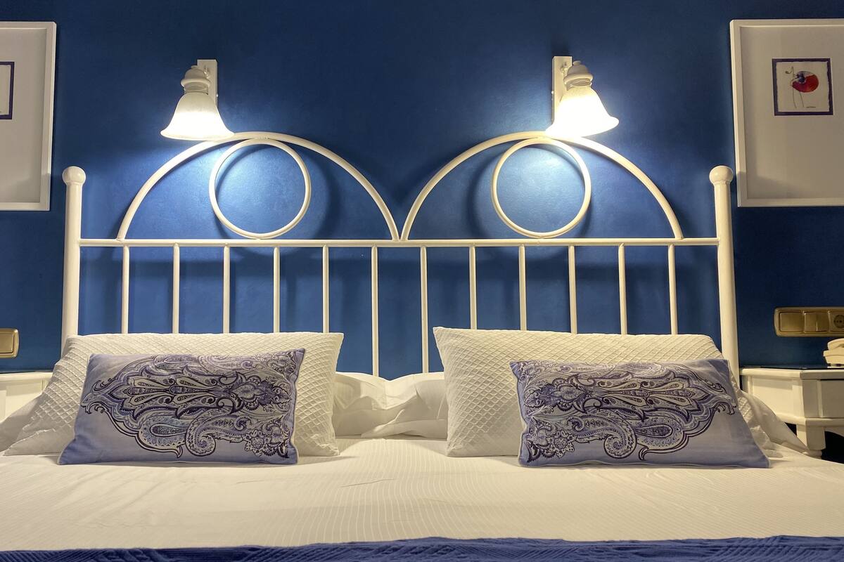 A bed with a white headboard and two wall-mounted lights, a bedside table with a phone, and two framed pictures on the wall.