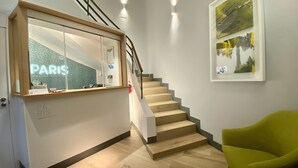 Uma escadaria com degraus de madeira e corrimão, levando a uma área de recepção com um painel de vidro exibindo 'PARIS HOSTAL BOUTIQUE'.