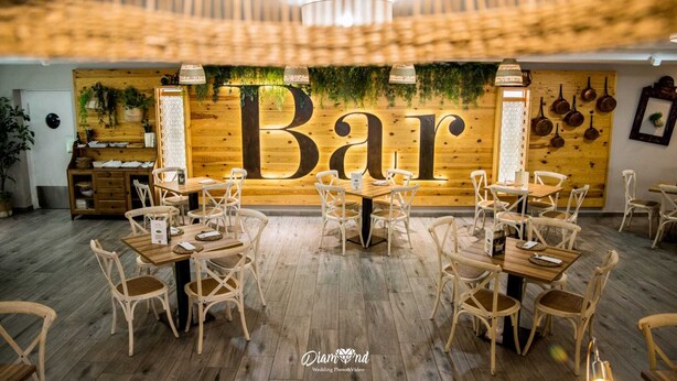 A restaurant interior with a large 'Bar' sign, wooden tables, wicker chairs, and a wooden ceiling. - Hotel Ínsula Barataria (Alcazar de San Juan)