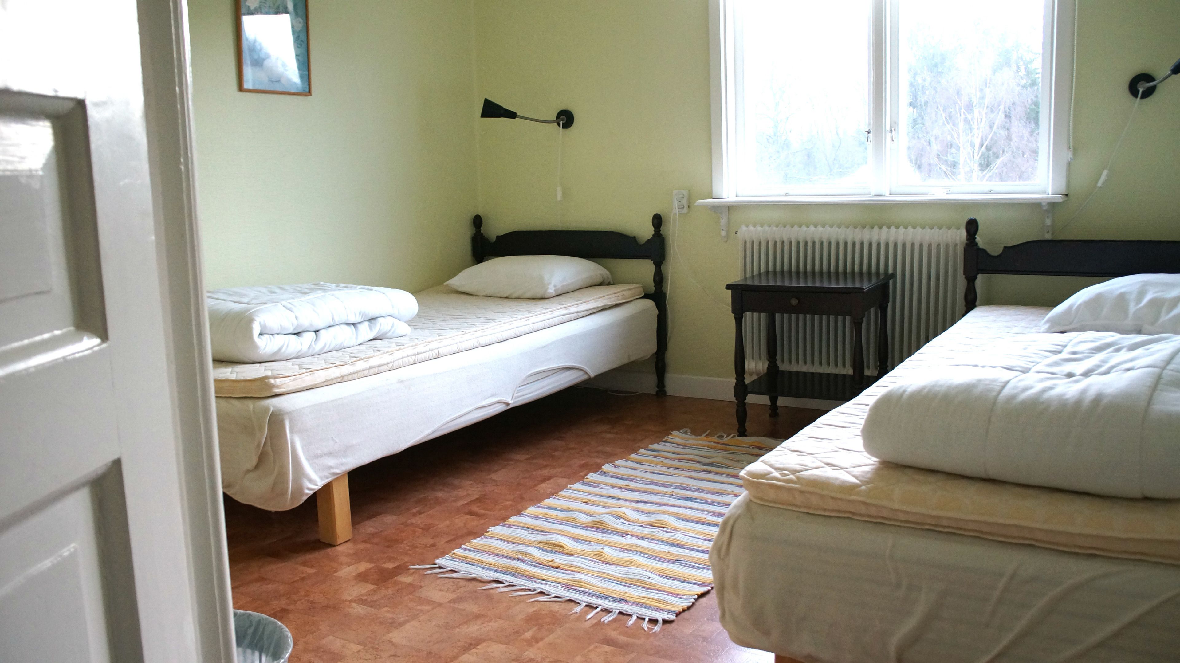 Een slaapkamer met twee bedden, een tafeltje, een radiator en een raam.