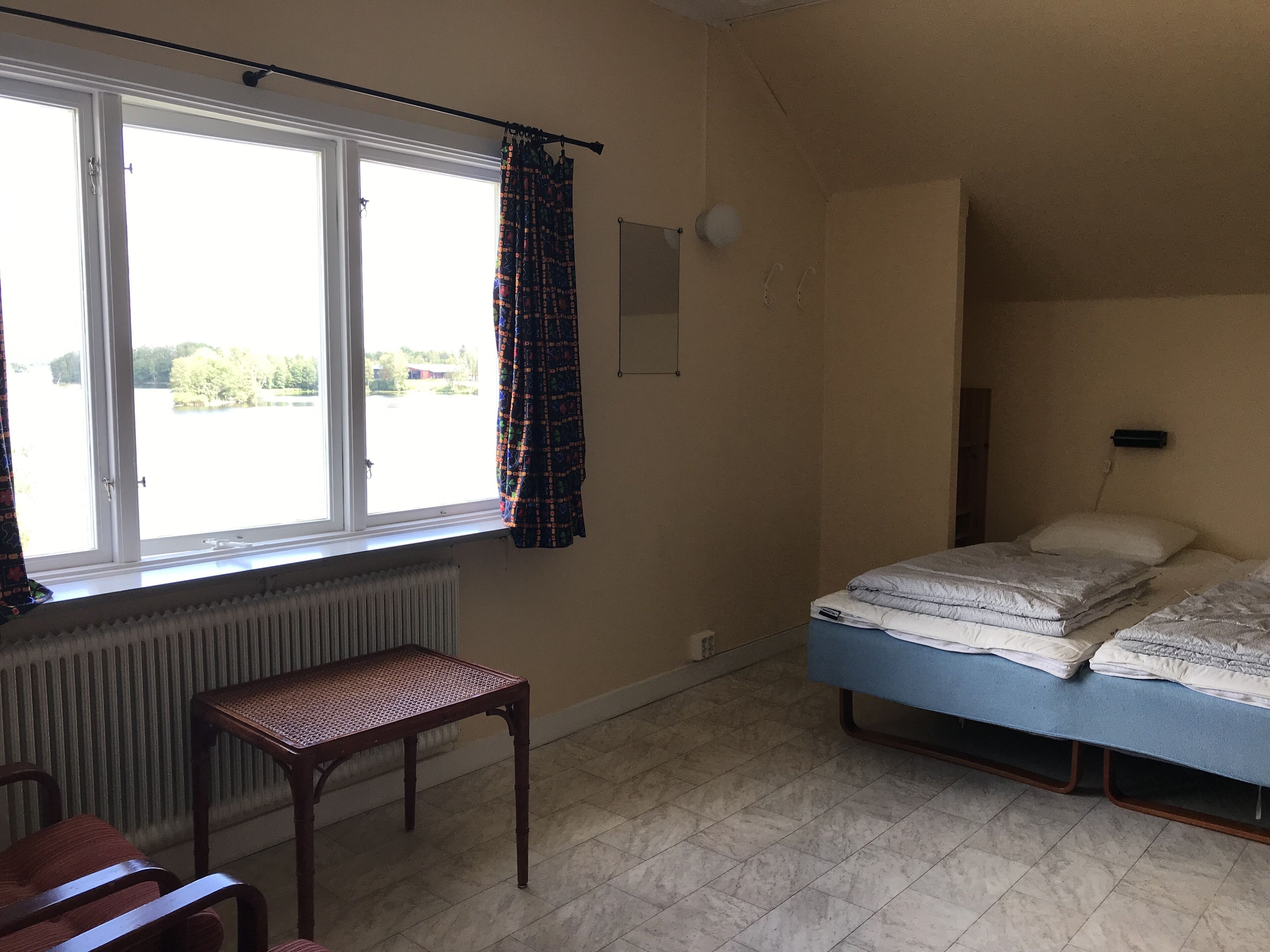A room with a bed, a chair, a radiator, and a window with curtains.