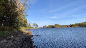 Vista de un lago con orilla rocosa, árboles y un edificio a lo lejos.