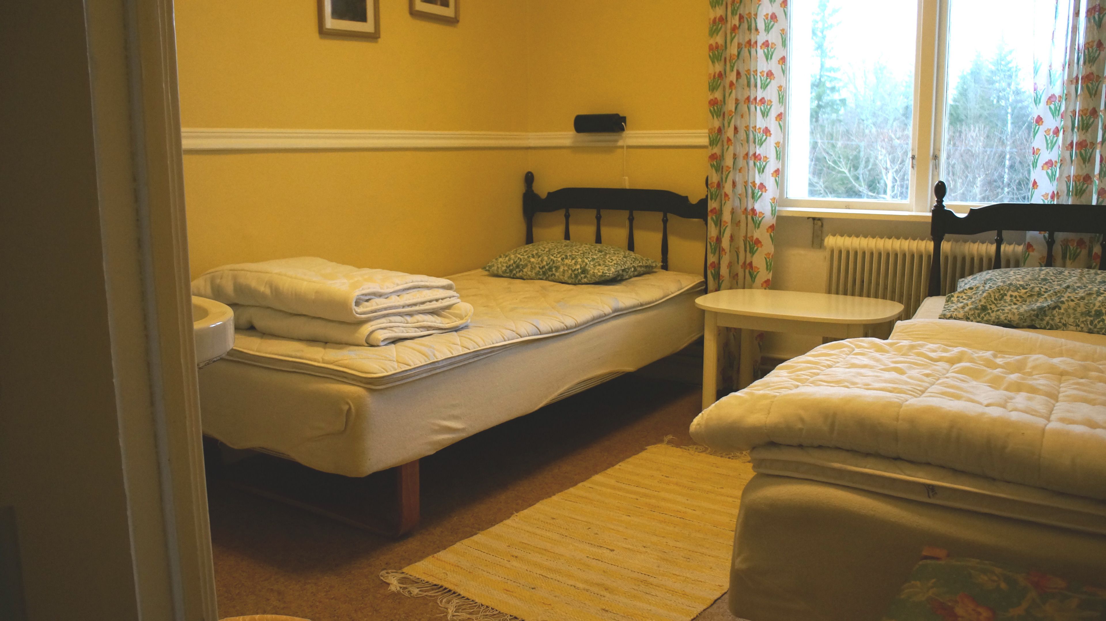 Una habitación con dos camas, una mesita y un ventanal con cortinas.