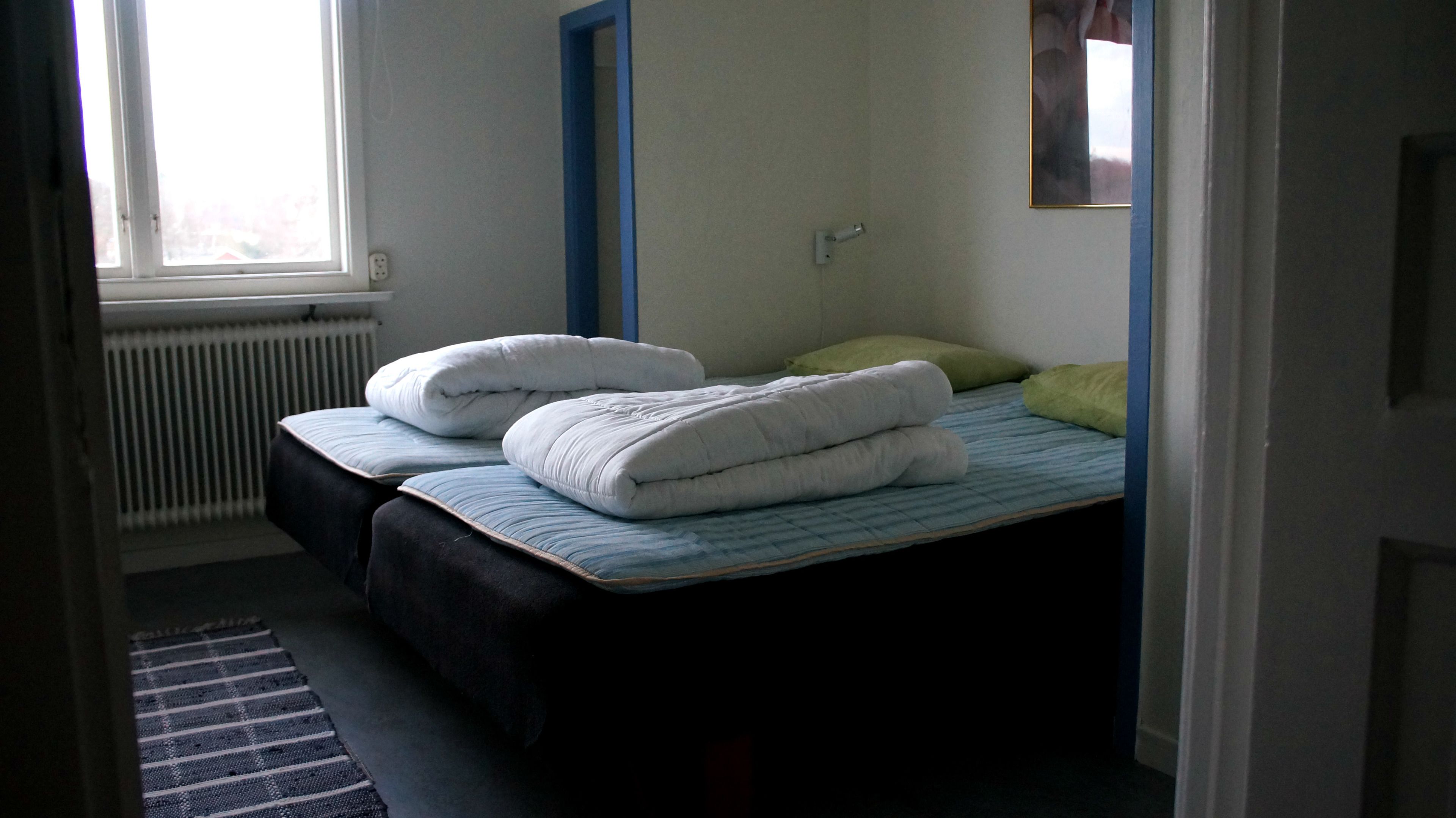 Quarto com duas camas, um radiador e uma janela.