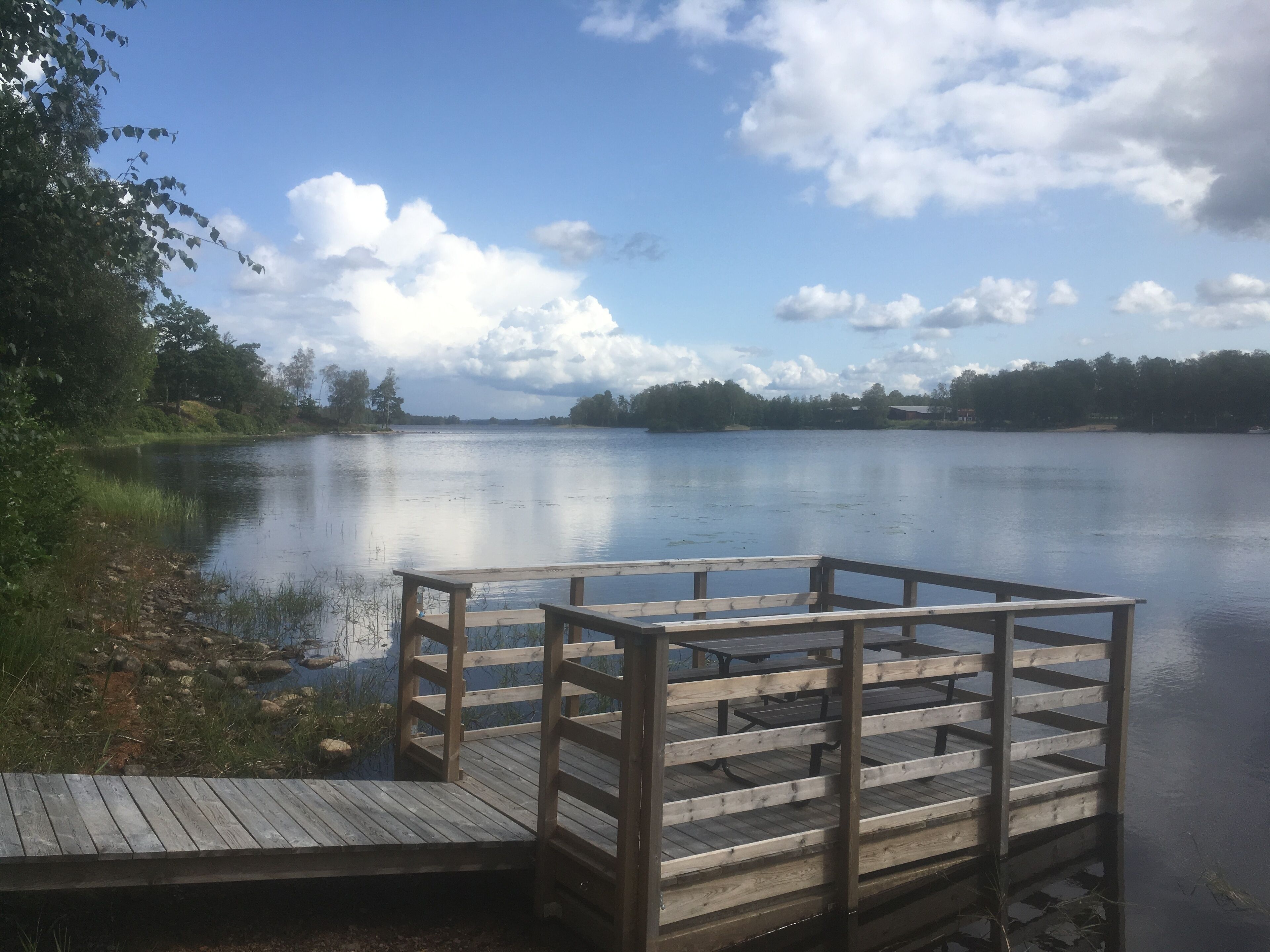 A wooden dock extending into a calm lake with trees and a clear sky in the background.