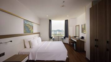A hotel room with a large bed, a desk, a chair, and a view of the city.