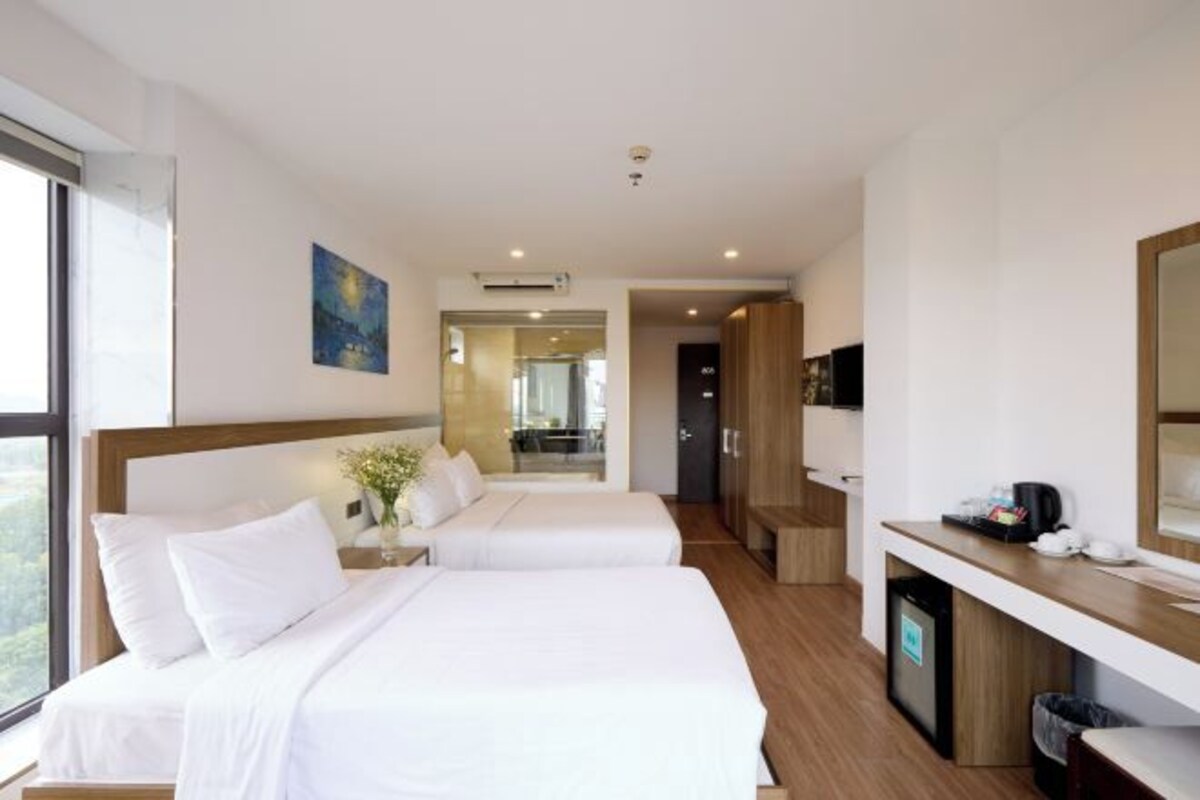 A hotel room with two beds, a desk, a TV, and a view of the outdoors.