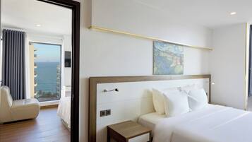 Ein Hotelzimmer mit einem großen Bett, einem Nachttisch, einem Sessel und Blick aufs Meer.