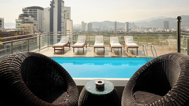Una piscina en la azotea con sillones de descanso y vistas a la ciudad.