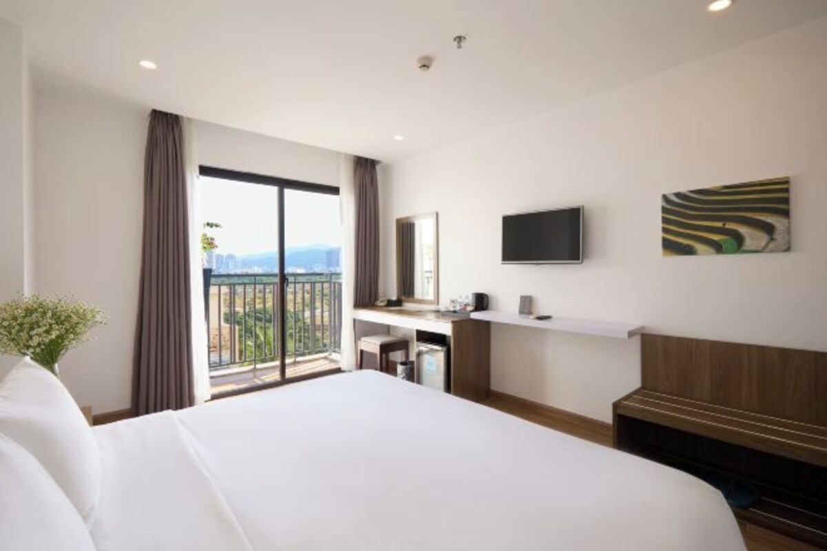 A hotel room with a large bed, a desk, a flat-screen TV, and a balcony with a view.