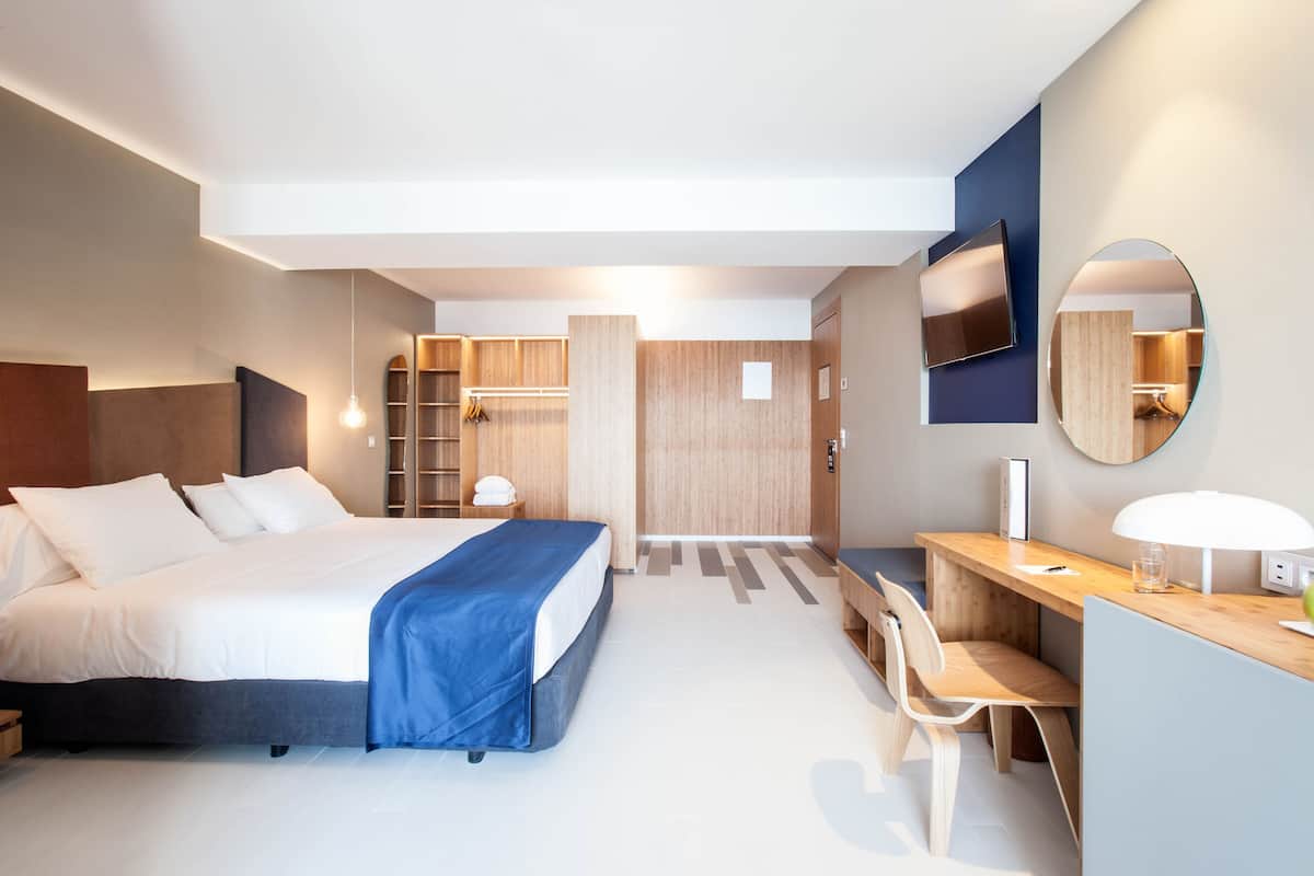 A modern hotel room with a large bed, a desk, a chair, a TV, and a mirror.