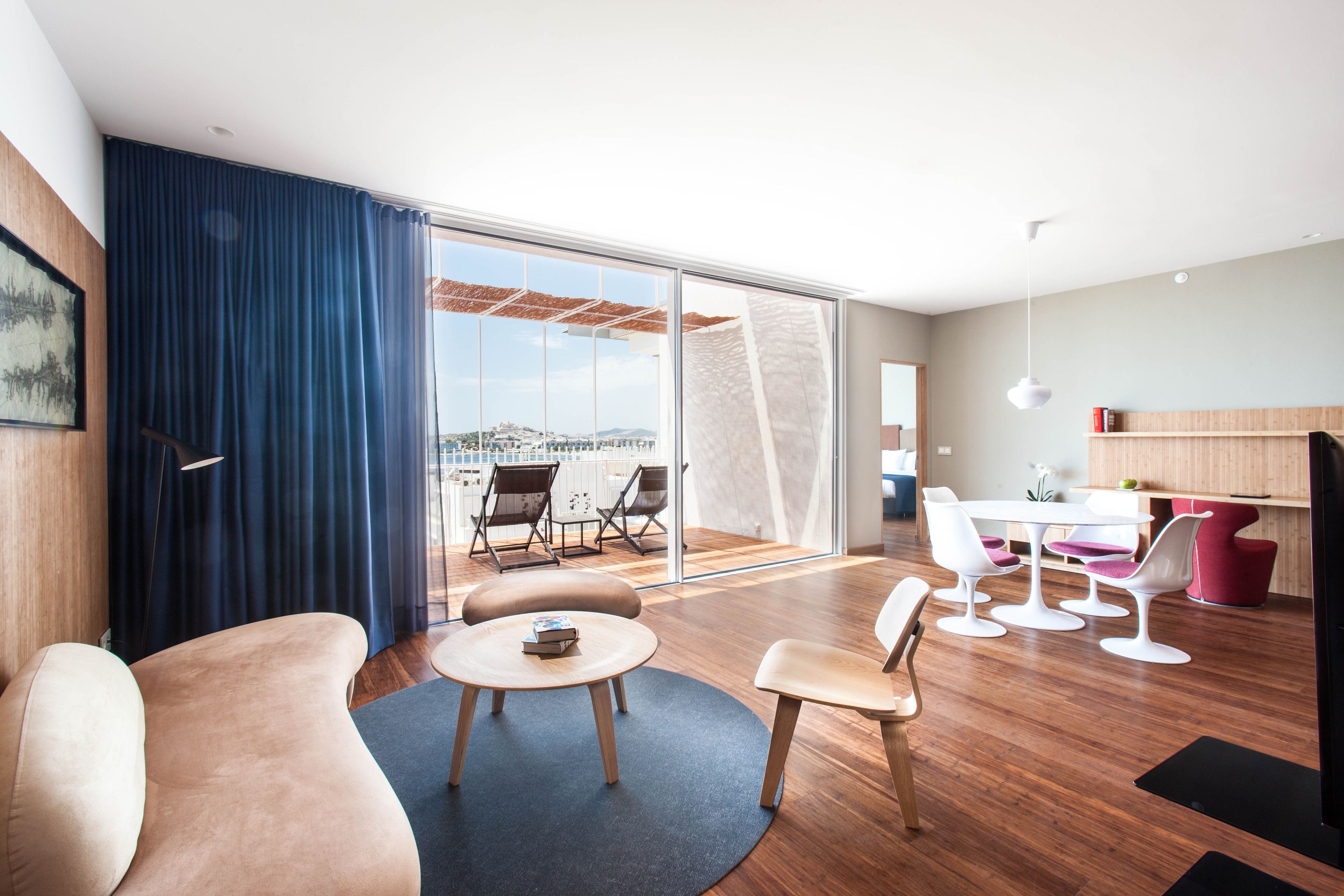 A modern living room with a sofa, a coffee table, and a dining area with white chairs and a table.