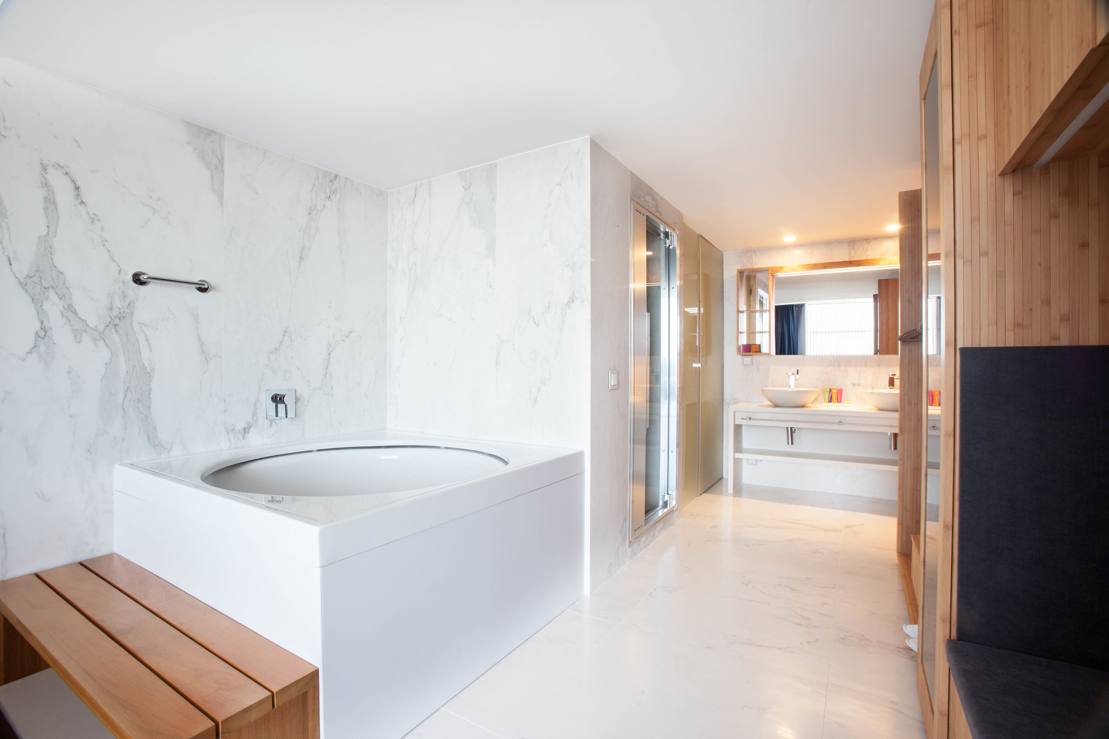 A modern bathroom with a large bathtub, marble walls, and wooden accents.