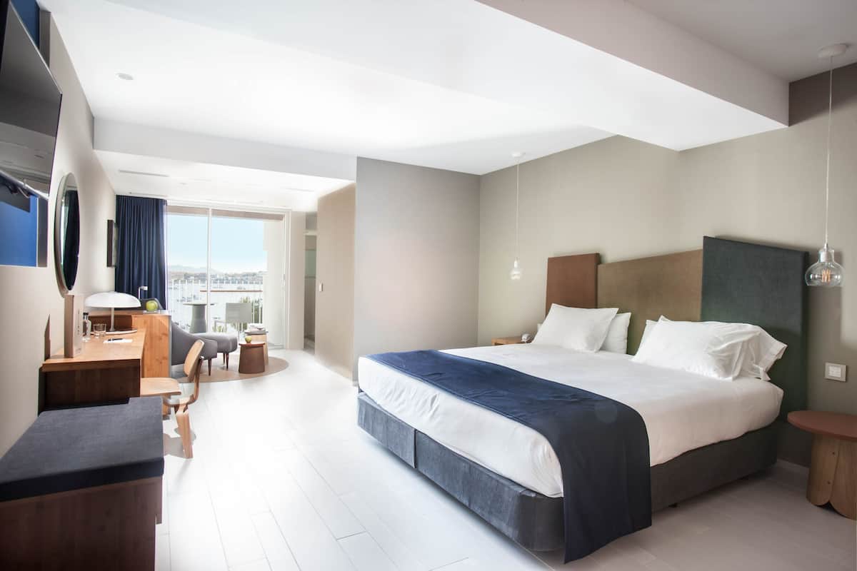 A modern hotel room with a large bed, a desk, and a view of the city.
