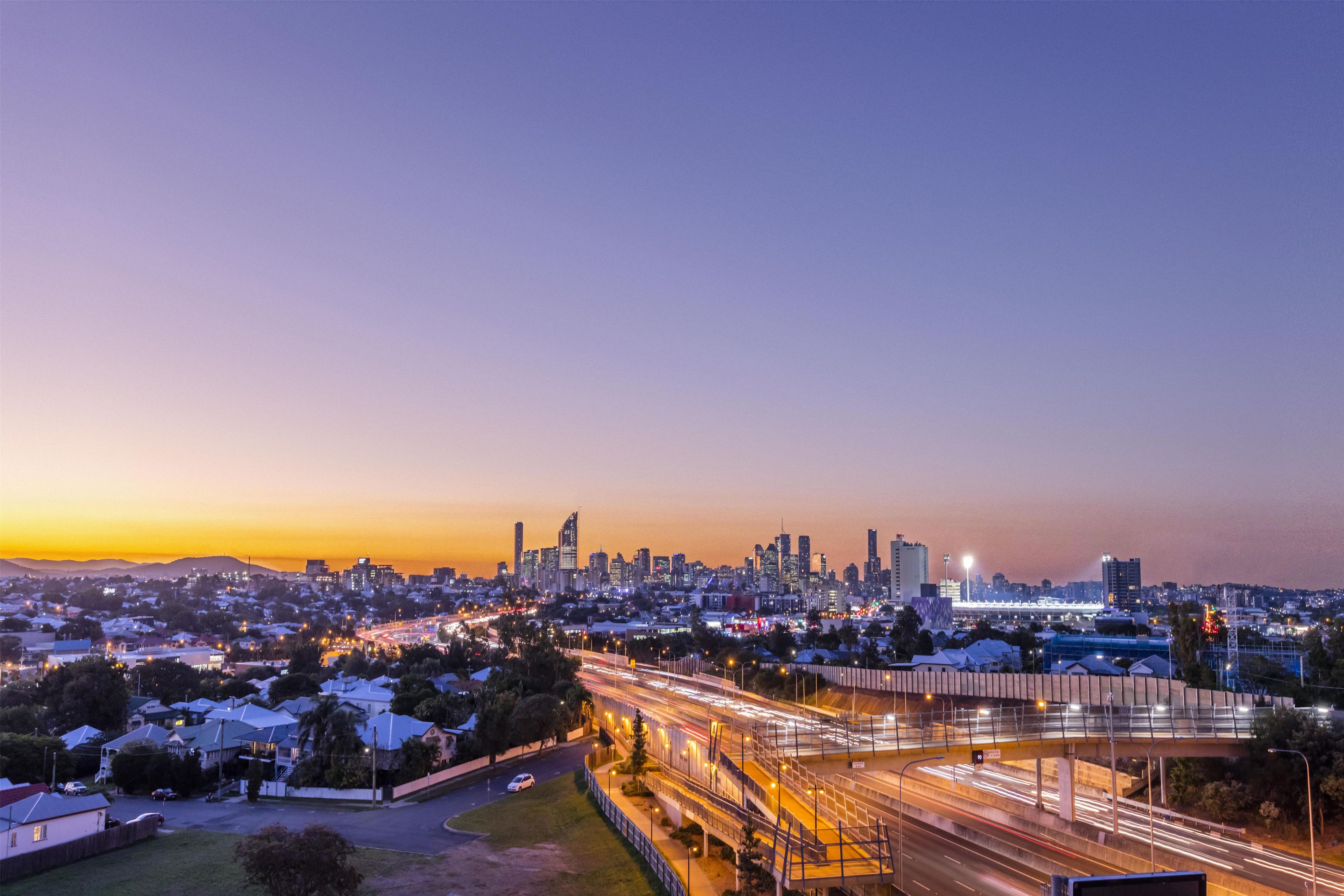 A cityscape at dusk with a prominent skyline, a highway with light trails, and residential areas.