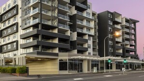 Un edificio residenziale a più piani con balconi, un ingresso coperto e vista sulla strada con un semaforo.
