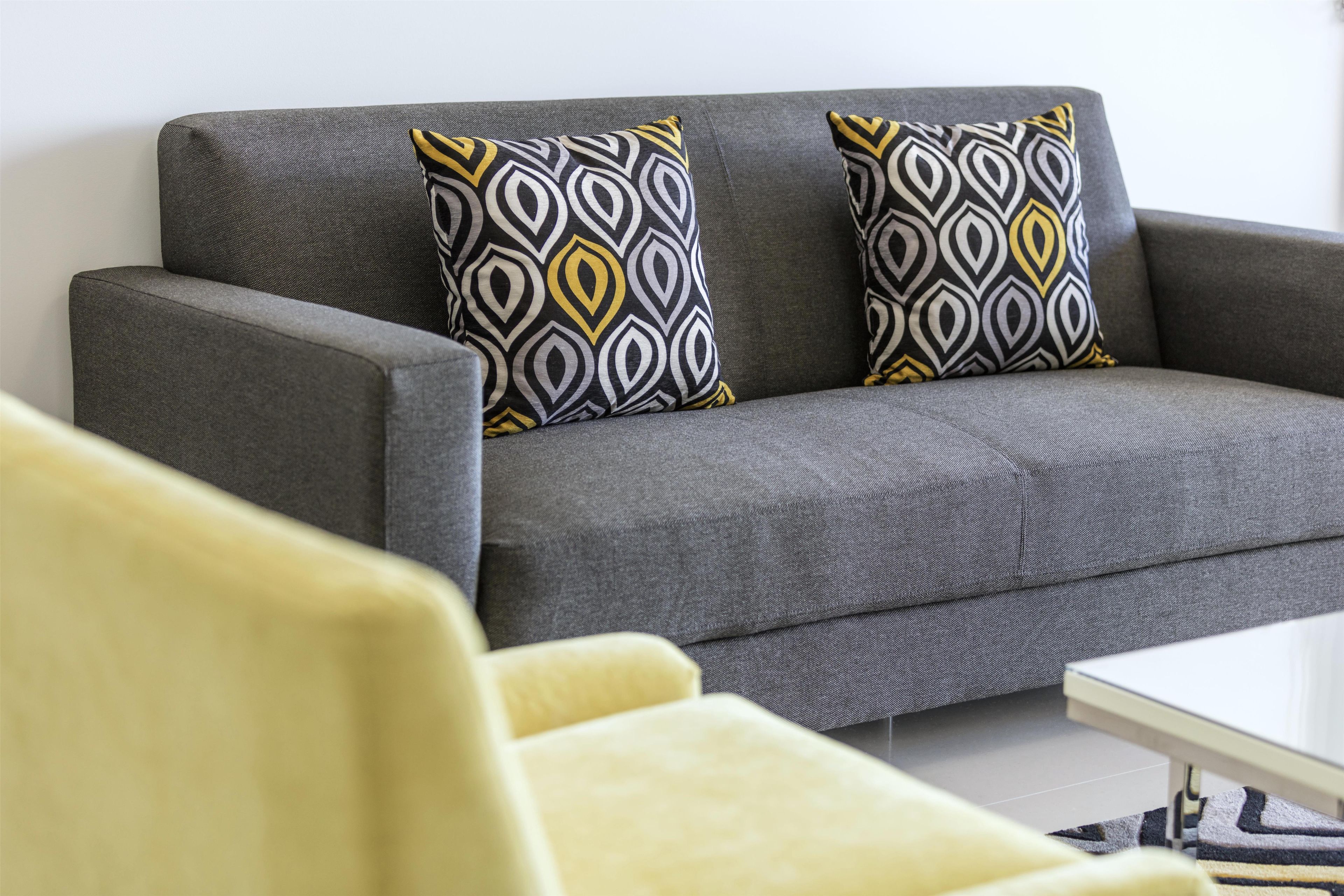 Un sofá gris con cojines estampados, un sillón amarillo y una mesa blanca en una sala de estar.