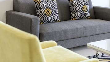 Un sofá gris con cojines estampados, un sillón amarillo y una mesa blanca en una sala de estar.