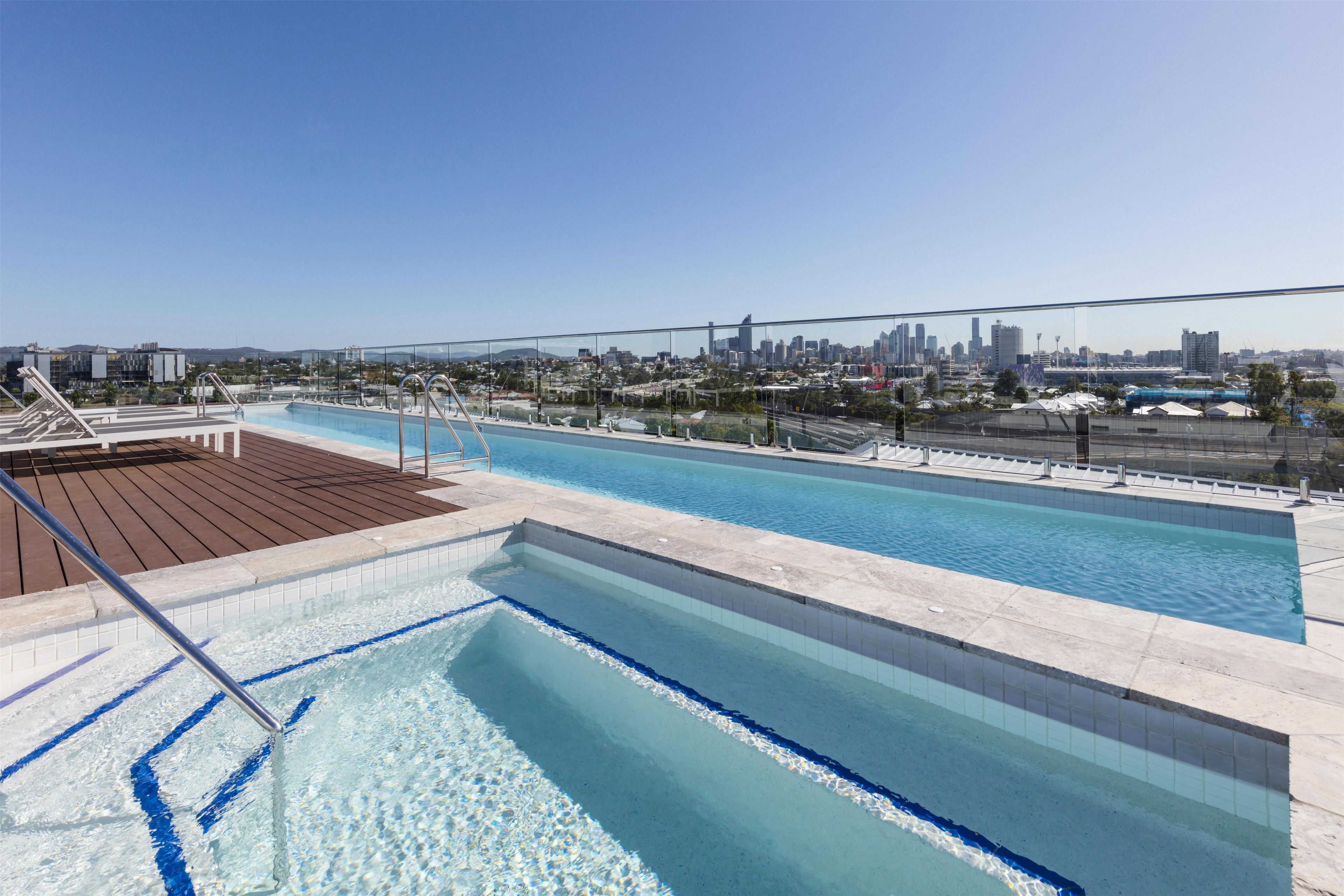 Una piscina sul tetto con vista sullo skyline cittadino, un pontile in legno e ringhiere metalliche.