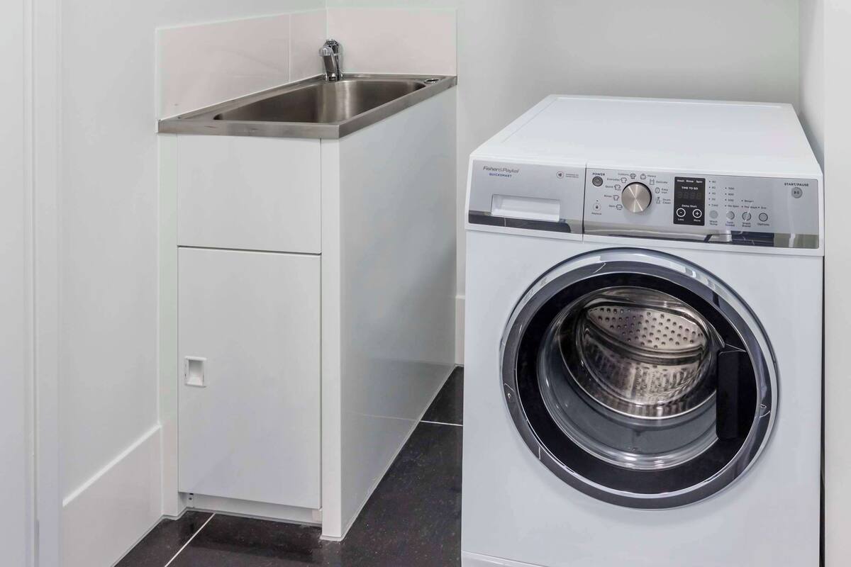 Un espace buanderie compact comprenant un lave-linge, un petit évier et un meuble de rangement.