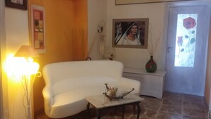 En stue med en hvid sofa, et lille bord med en pynteting, en lampe, et billede på væggen og en vase med blomster.