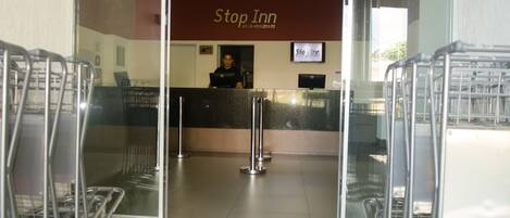 Una zona de recepción con un letrero de 'Stop Inn', un recepcionista y varios carritos de compras.