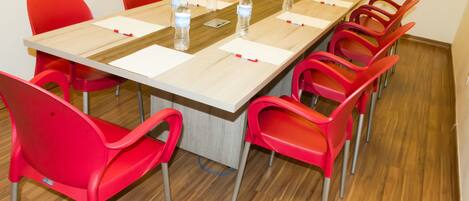 Une salle de conférence avec une longue table, des chaises rouges, des bouteilles d’eau et des blocs-notes.