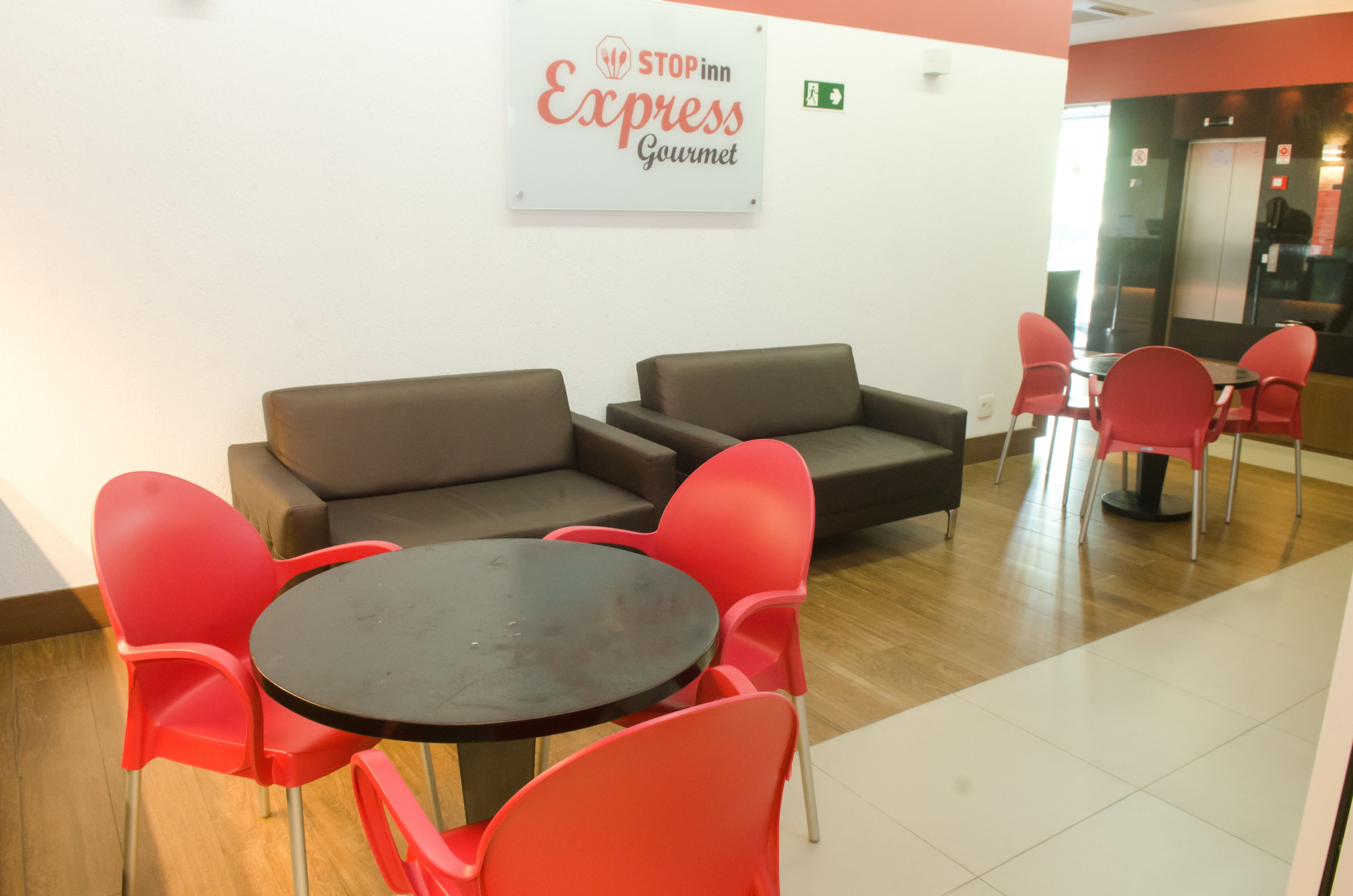 A reception area with a brown sofa, red chairs, a small round table, and a sign that reads "STOPinn Express Gourmet".