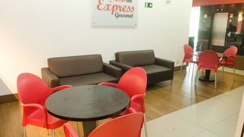 A reception area with a brown sofa, red chairs, a small round table, and a sign that reads "STOPinn Express Gourmet".
