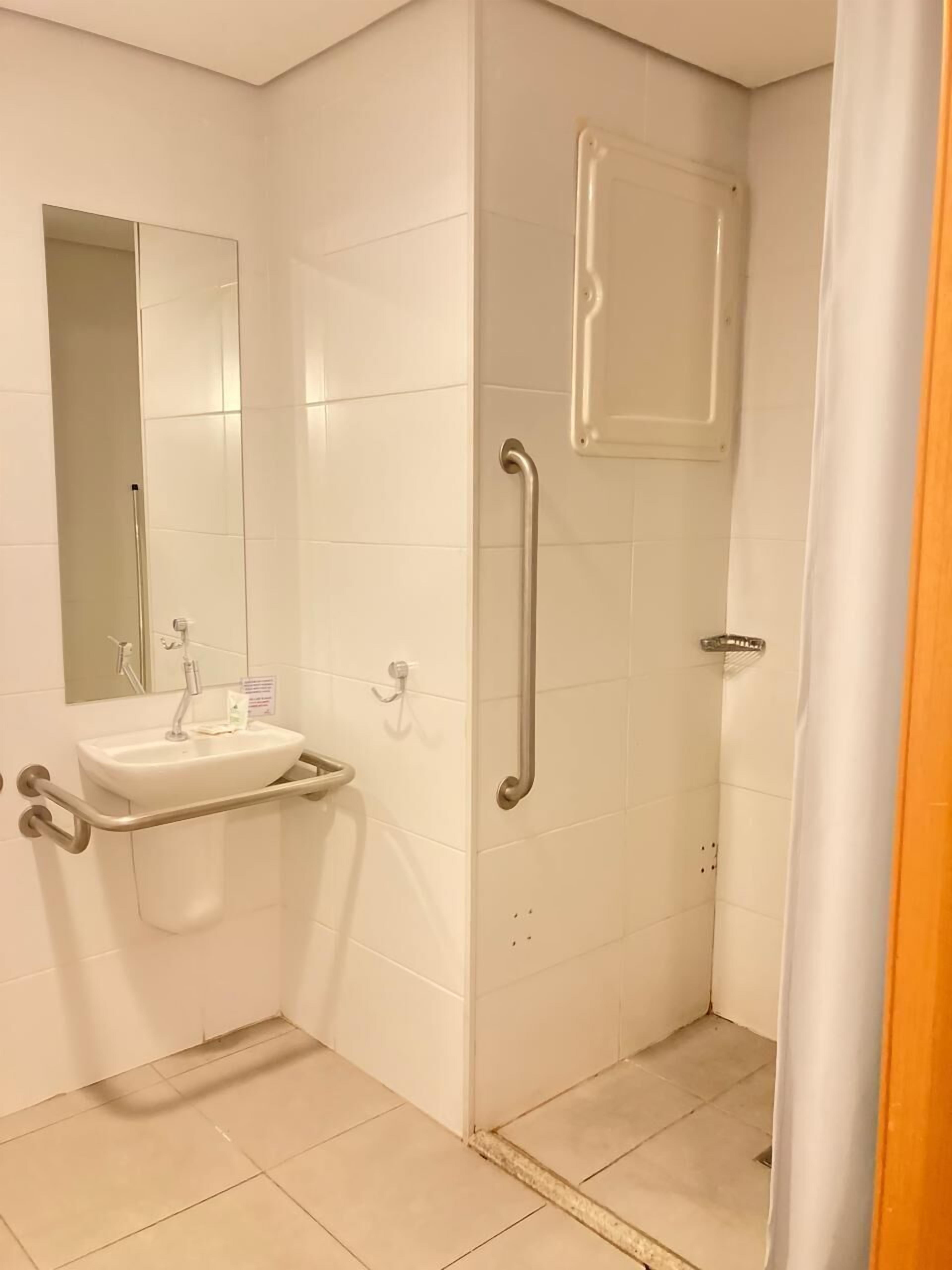 Ein Badezimmer mit Waschbecken, Spiegel und Dusche mit Haltegriff.