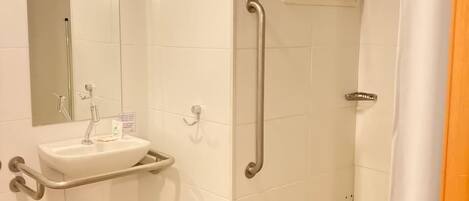 Ein Badezimmer mit Waschbecken, Spiegel und Dusche mit Haltegriff.