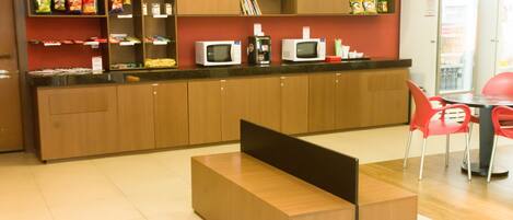 A modern kitchen area with wooden cabinets, a countertop with microwaves, and a seating area with red chairs.