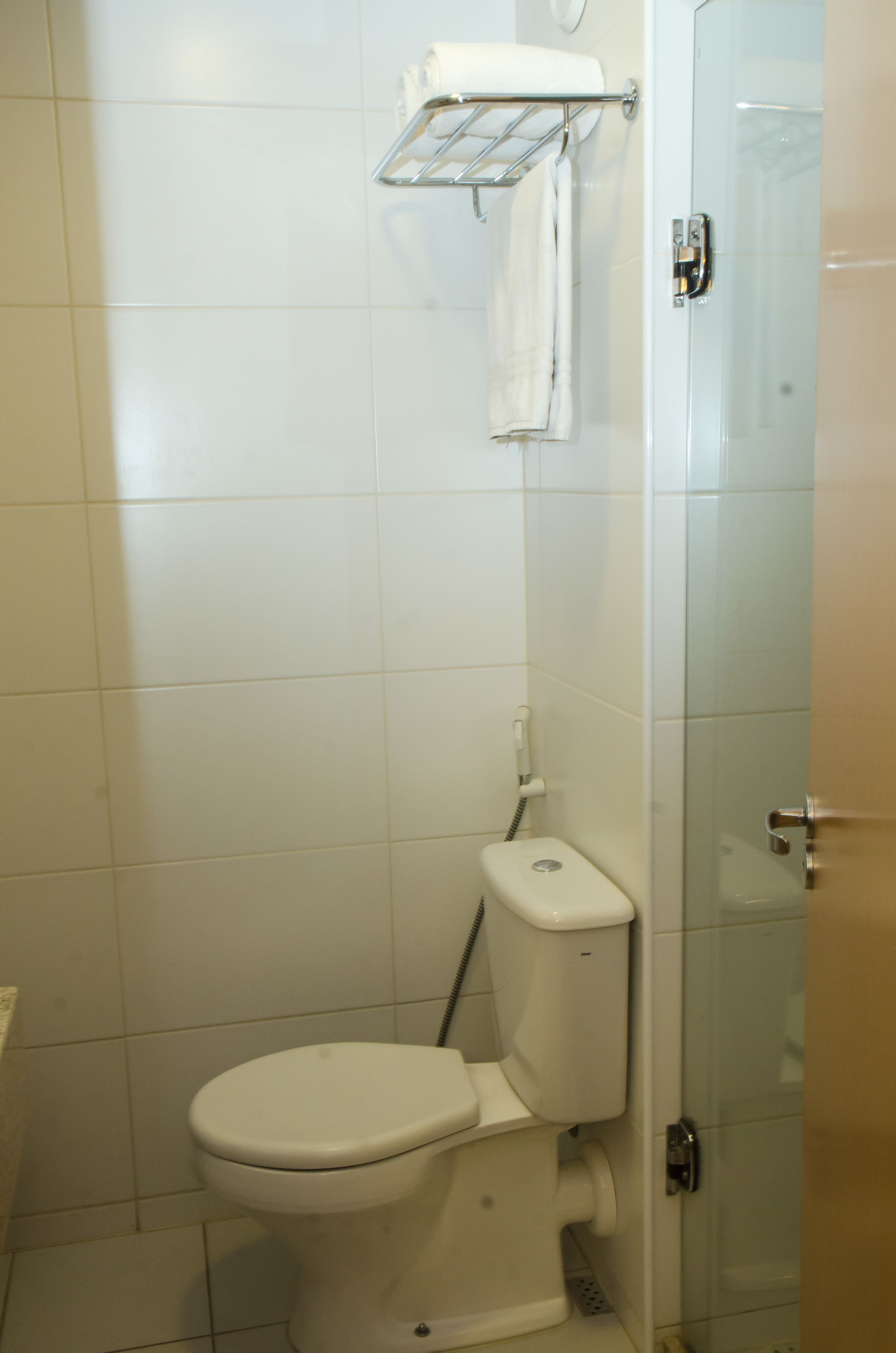 Un baño pequeño y moderno con inodoro, cabina de ducha de vidrio y un perchero para toallas.