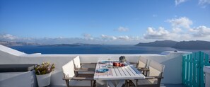 A table set with plates, cutlery, and a glass of white wine, overlooking a scenic view of the sea and distant land. -  Cave Agapi Oia (Santorini)