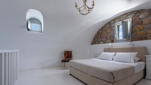 Un dormitorio con una cama grande, una ventana pequeña, una silla y una pared de piedra.