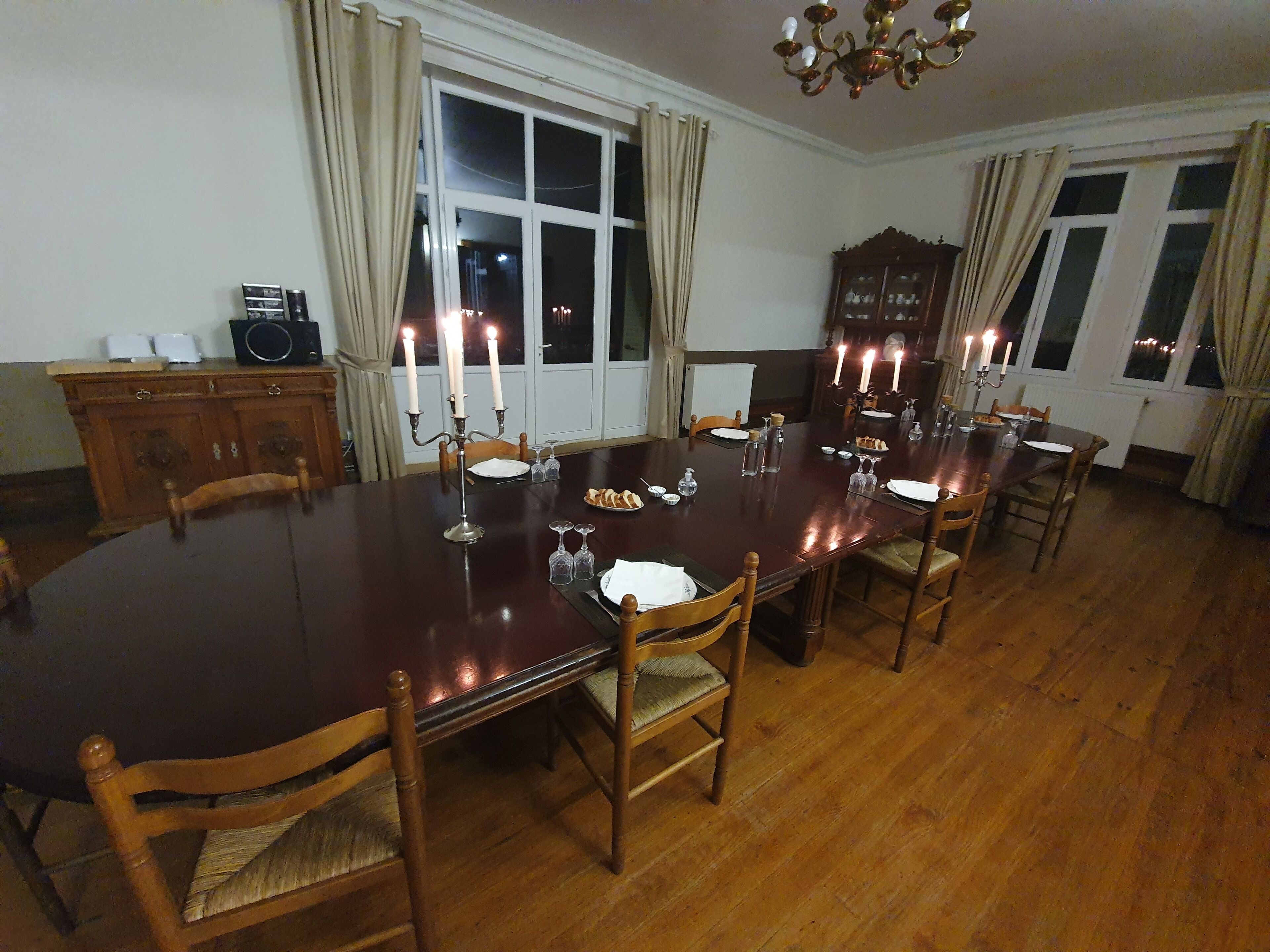 A dining room with a large wooden table set for six, surrounded by wooden chairs.