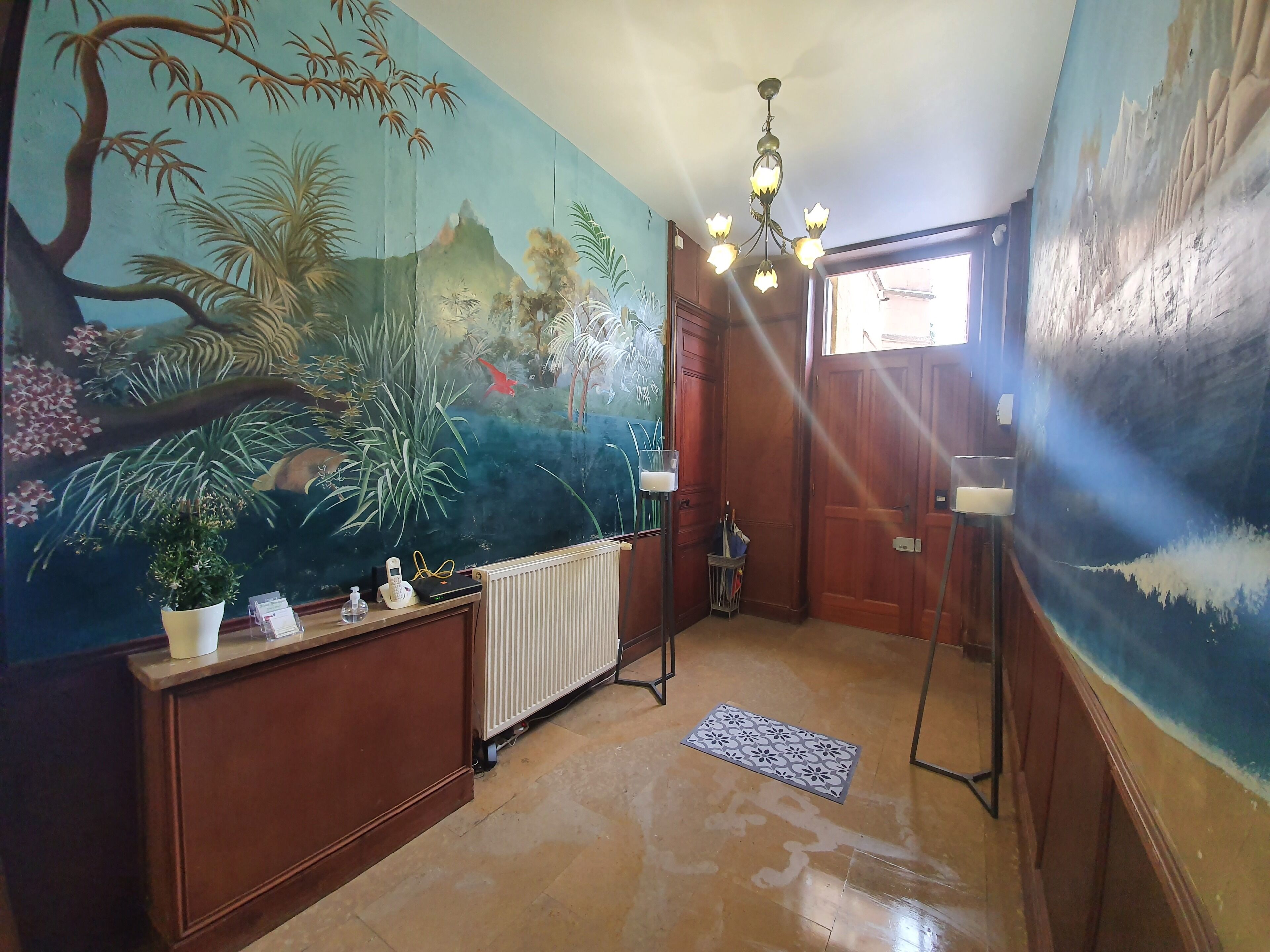 Quarto com um grande mural de paisagem tropical, um armário de madeira, um radiador e uma porta que dá para o exterior.