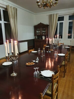 Une salle à manger avec une longue table en bois, dressée pour un repas, entourée de chaises.
