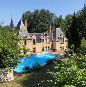Un grand bâtiment historique doté d’une piscine, entouré d’une végétation luxuriante.