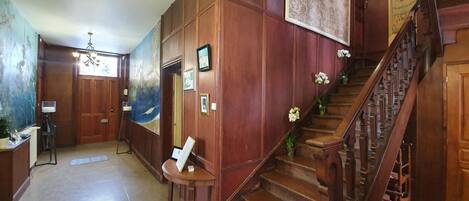 A grand hallway with wooden paneling, a staircase, and a large painting on the wall.
