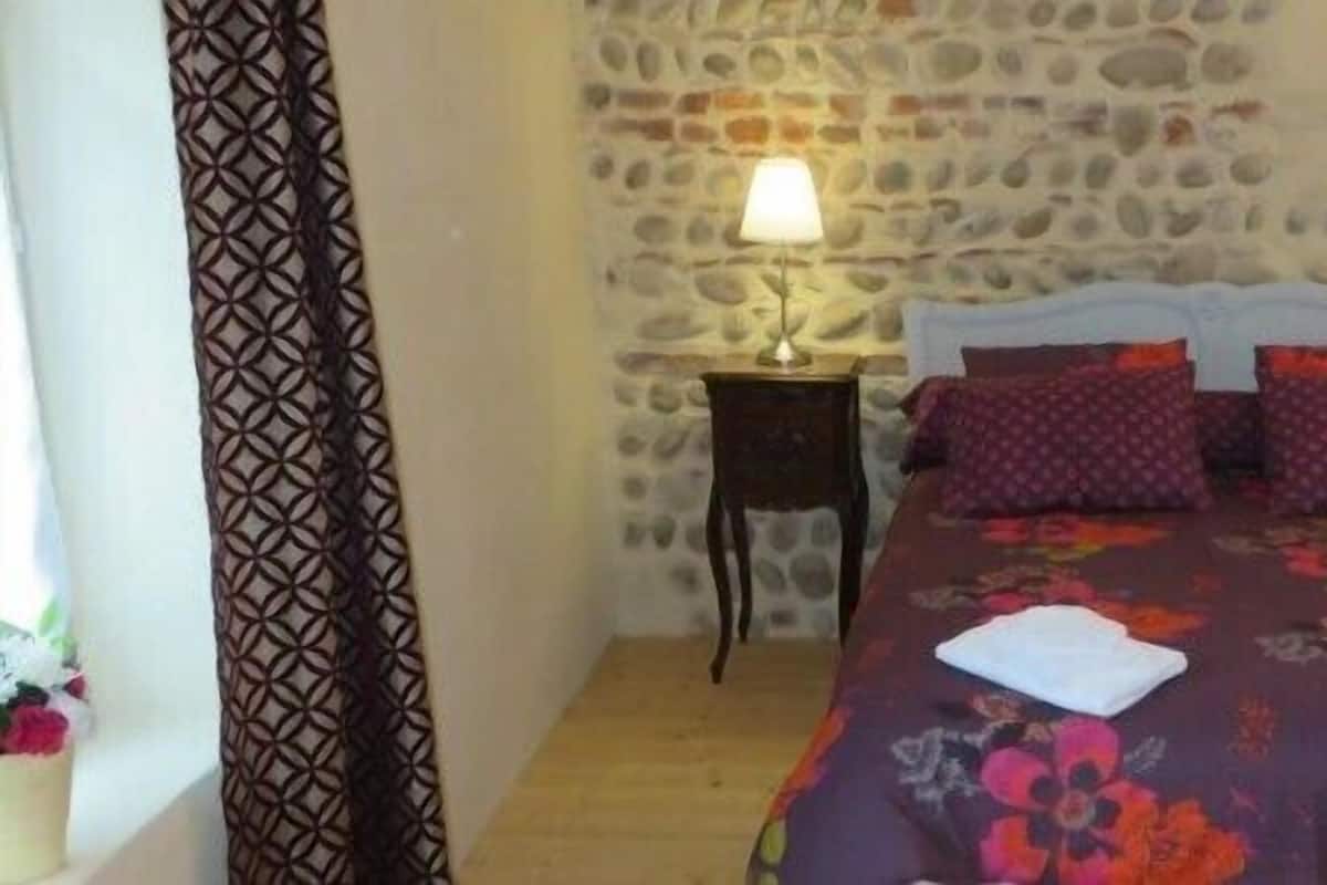 Un dormitorio con pared de piedra, una cama con cubrecama floral, dos lámparas de noche y piso de madera.