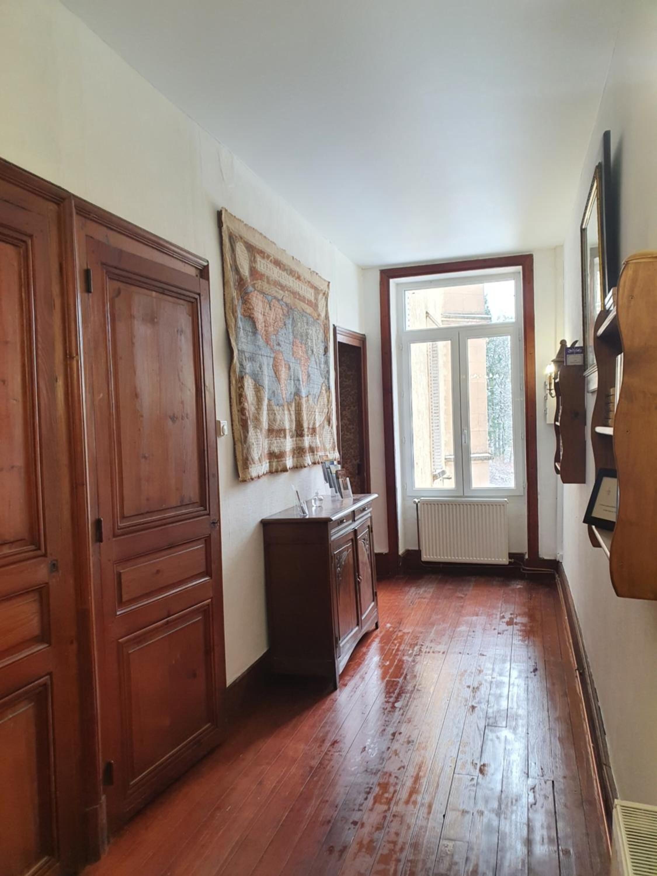Un passadís amb terres de fusta, un mapa del món gran a la paret i un radiador a prop d'una finestra.