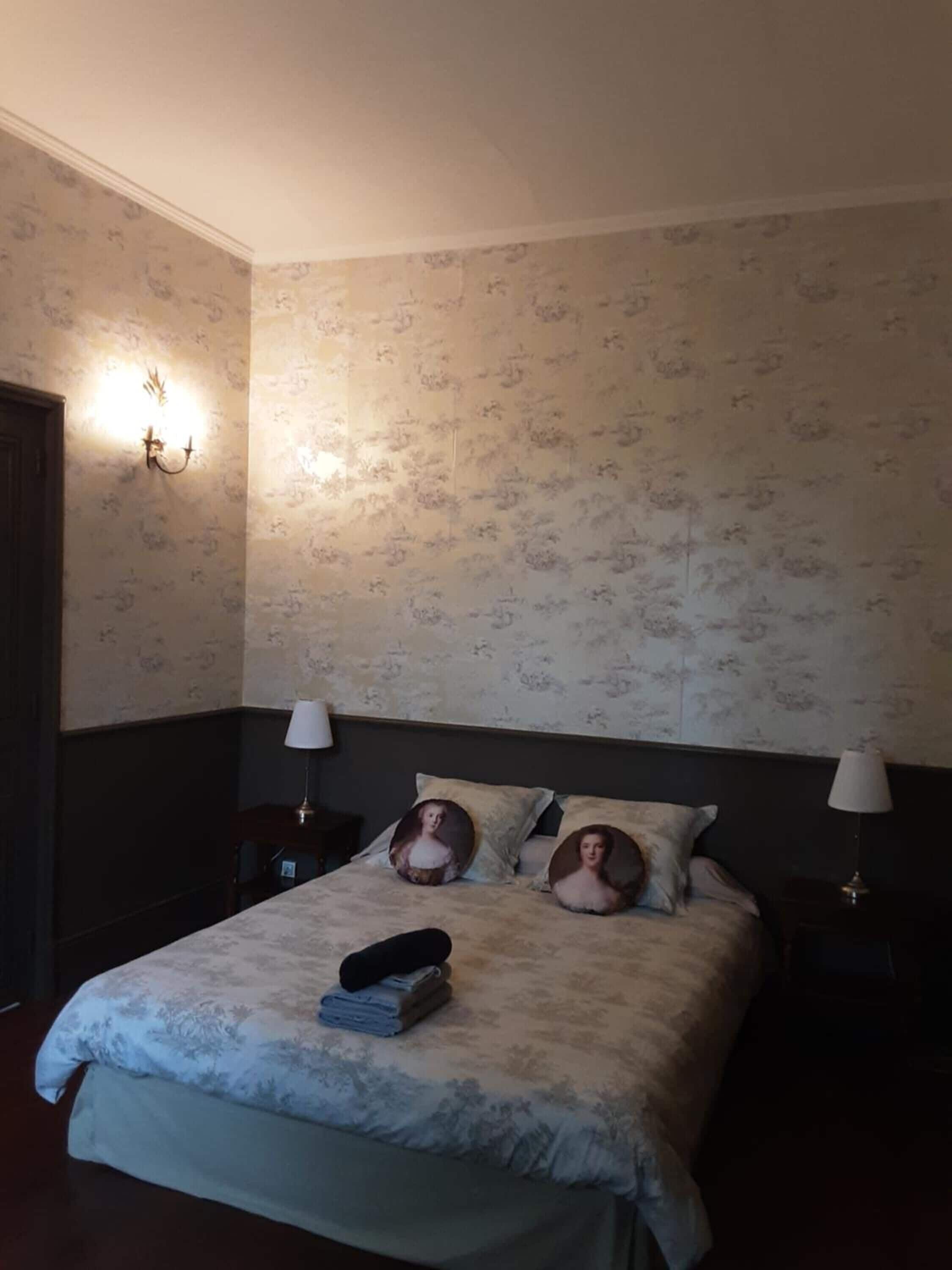 A bedroom with a bed, two bedside lamps, a nightstand, and a wall-mounted light fixture.