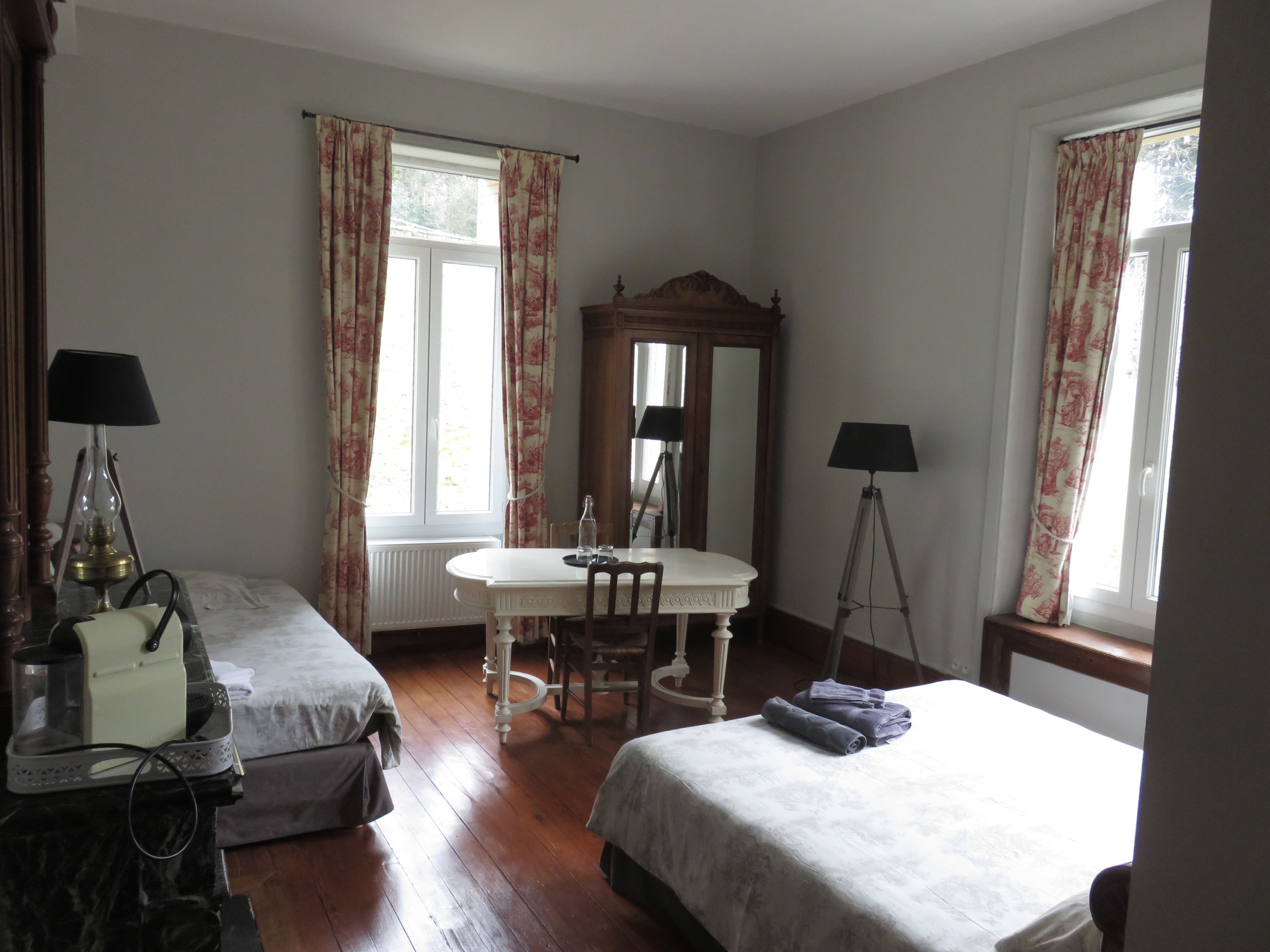 A hotel room with two beds, a dining table, a mirror, and two lamps.