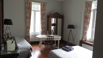 A hotel room with two beds, a dining table, a mirror, and two lamps.