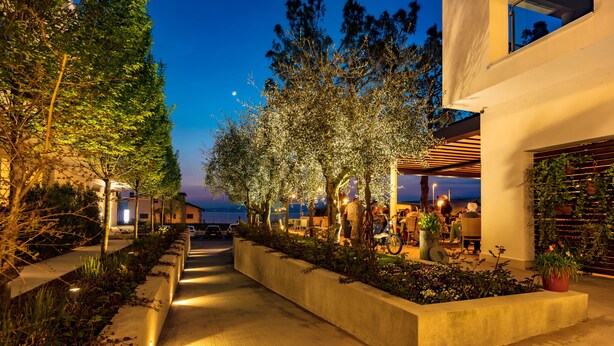 A nighttime outdoor area with a pathway, trees, and a seating area with tables and chairs. - Hotel Maximilian (Bardolino)