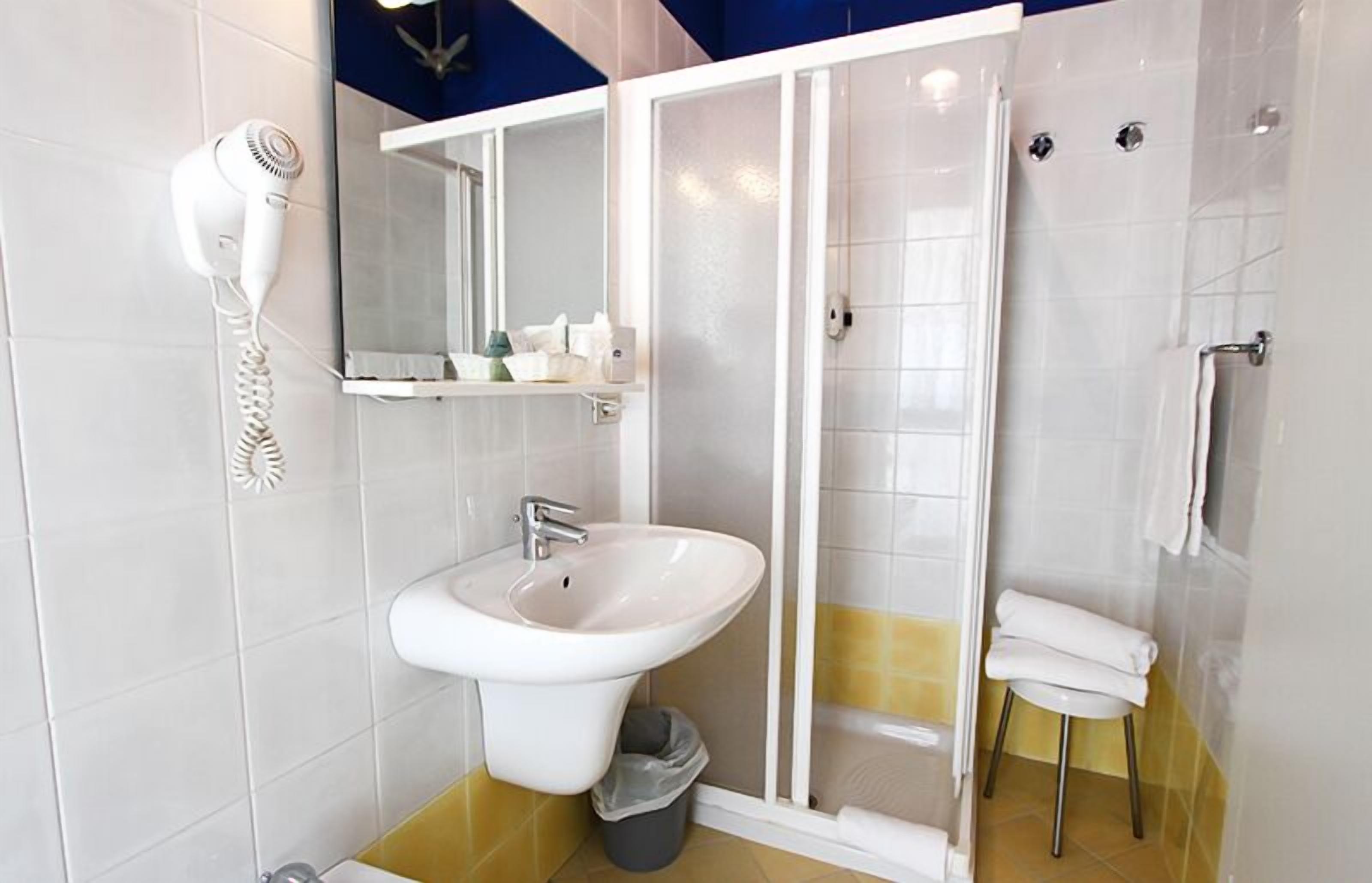 A bathroom with a white sink, a hairdryer, a mirror, a shower enclosure, and a towel rack.