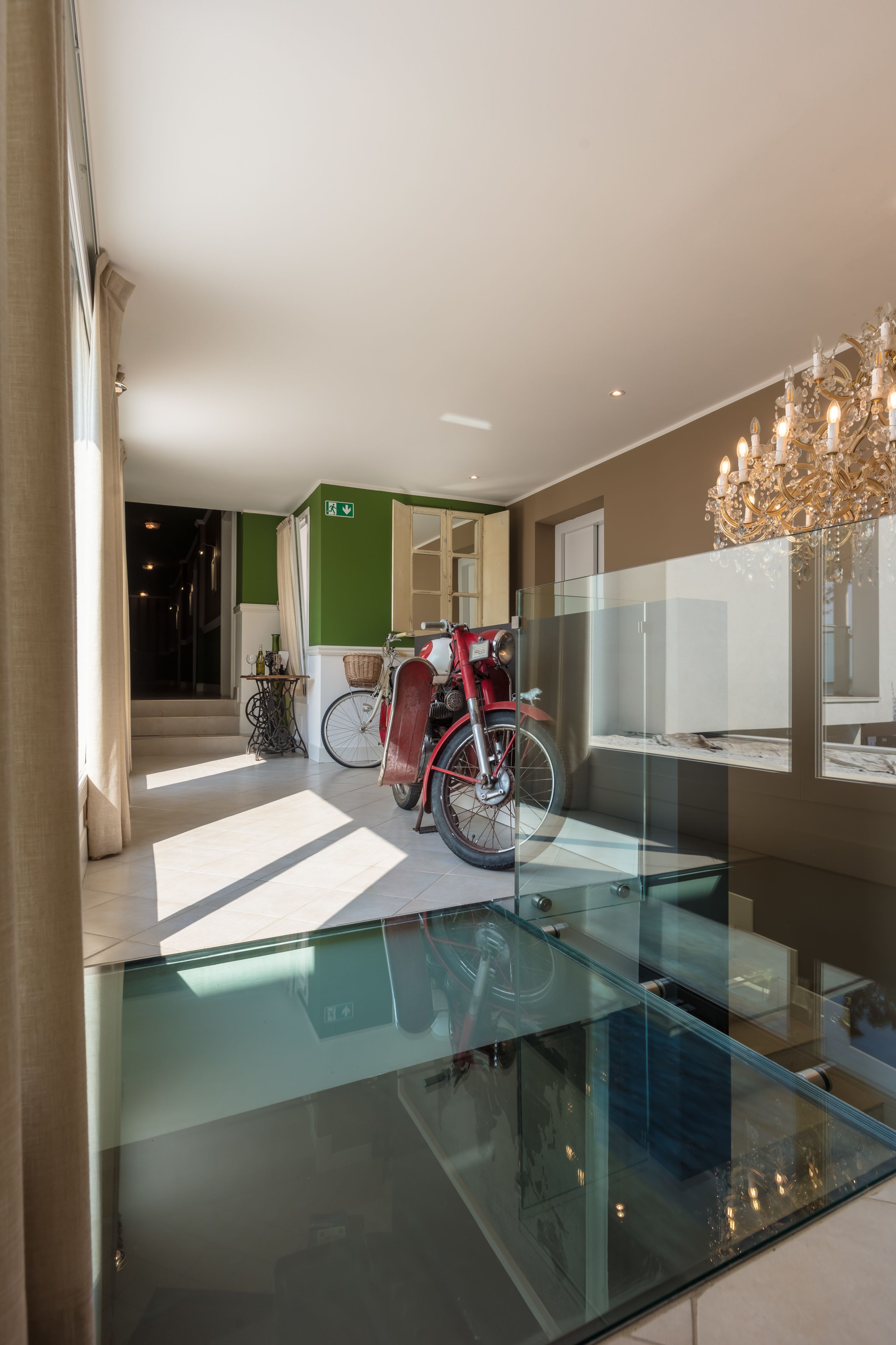 A modern hotel lobby with a glass floor, a red vintage motorcycle, and a chandelier.
